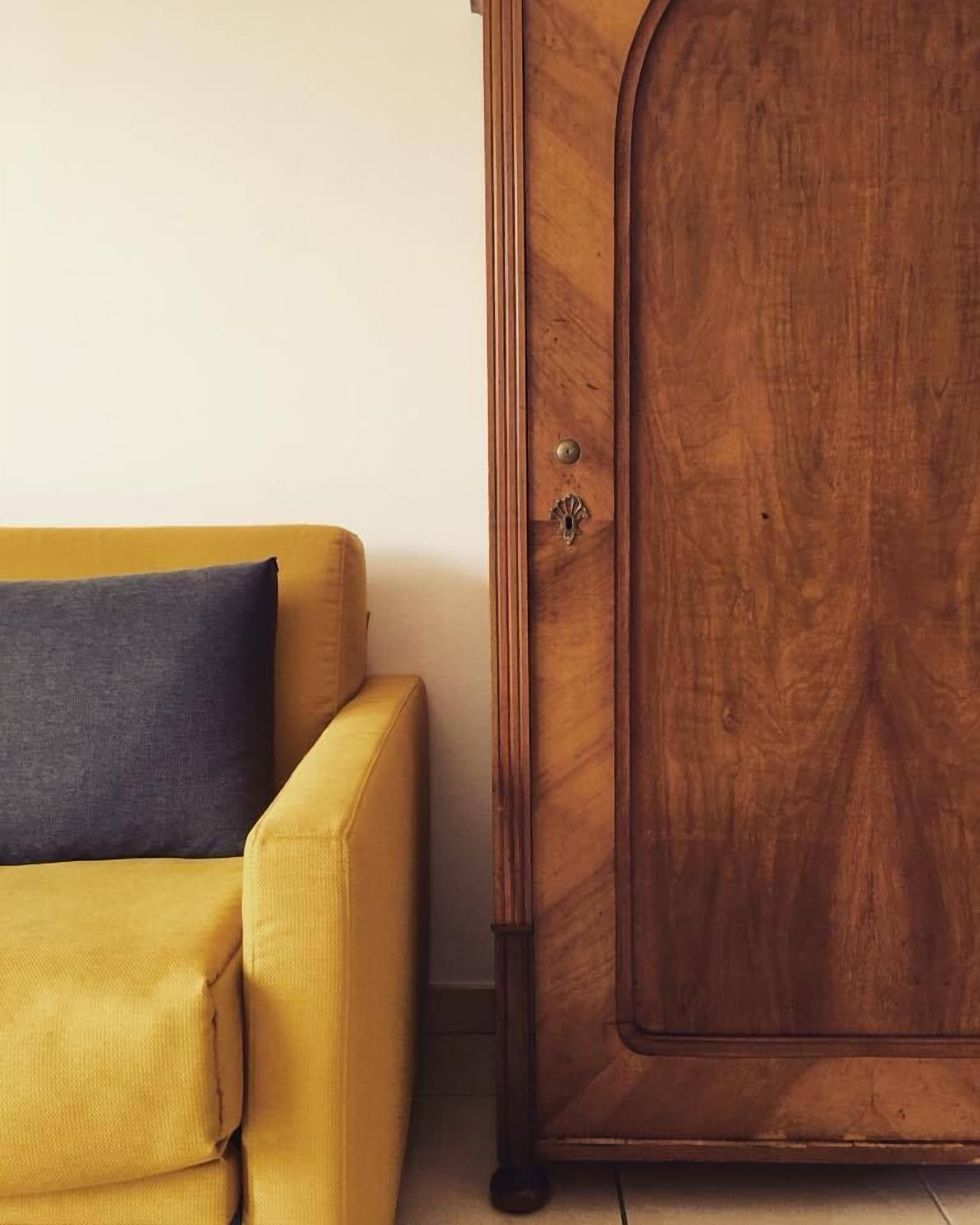 A yellow sofa with a dark cushion against a plain wall.