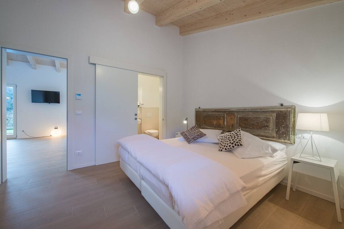 A bedroom with a bed, bedside table, lamp, and a television on the wall.