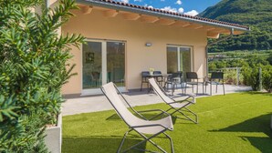 A modern house with a patio area featuring two lounge chairs, a table, and a glass door leading to an indoor space. - La Gazza Ladra Apartments (Drena)