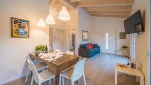 A modern living room with a dining area, wooden ceiling beams, a flat-screen TV, and a painting on the wall. - La Gazza Ladra Apartments (Drena)
