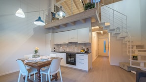 A modern kitchen with white cabinets, a wooden dining table, and pendant lighting. - La Gazza Ladra Apartments (Drena)