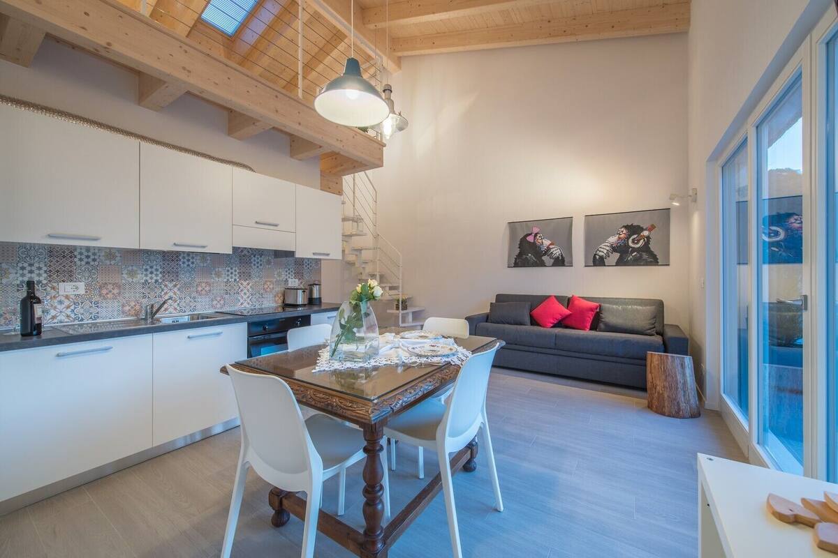 A modern kitchen with a dining area, a sofa with red cushions, and artwork on the wall.