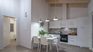 A modern kitchen with white cabinets, a dining table with chairs, and pendant lights. - La Gazza Ladra Apartments (Drena)