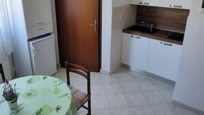 A compact kitchen with white cabinets, a wooden door, and a dining area with a table and chairs. - Apartment 2000/28358 (Istria - Fažana), 50m from the beach (Fažana)