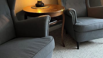 Un rincón con asientos, una mesa redonda de madera, una vela encendida y una alfombra estampada.