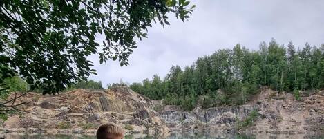 Une personne assise sur un rocher, au bord d’un lac aux eaux claires, avec une forêt en arrière-plan.