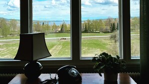 Una habitación con un ventanal grande, un escritorio con lámpara, un teléfono y una planta en maceta.