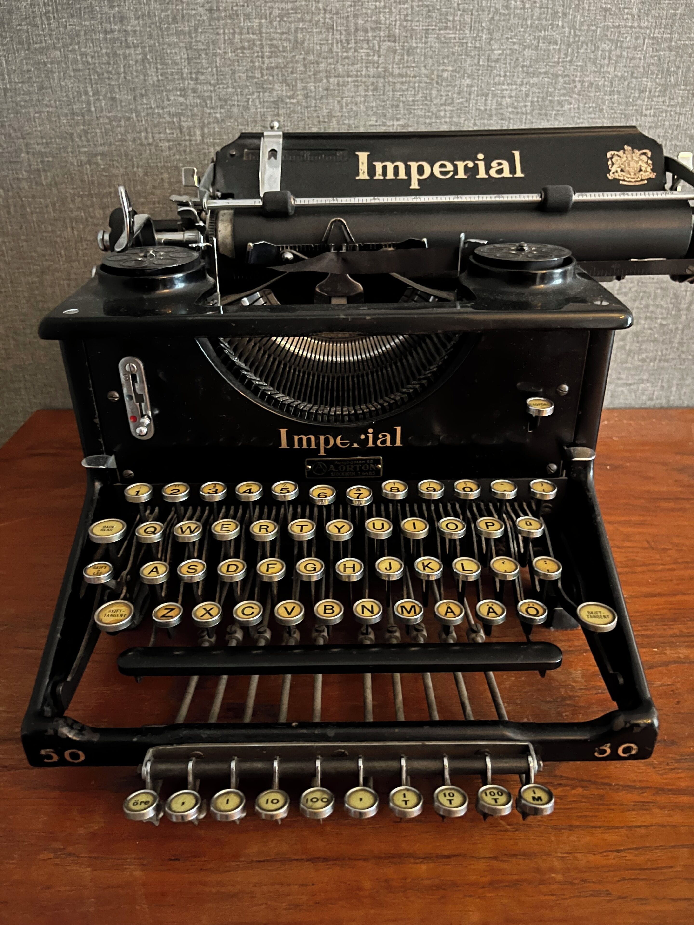 En klassisk skrivmaskin av märket Imperial, med svart stomme och guldfärgade detaljer, utrustad med ett QWERTY-tangentbord och en spak för att återställa vagnen.