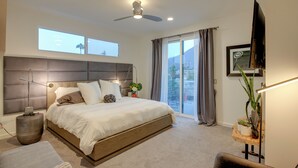 Un dormitorio moderno con una cama grande, ventilador de techo, televisor y balcón con cortinas.