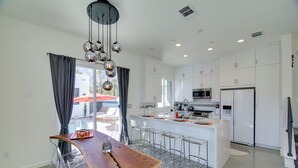 Cocina moderna con armarios blancos, una isla central con taburetes y una lámpara colgante, con vista a una piscina exterior.