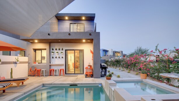 Una casa moderna con piscina, mobiliario exterior y plantas en macetas.