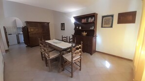 A dining area with a wooden table and chairs, a bookshelf, and a kitchen in the background.