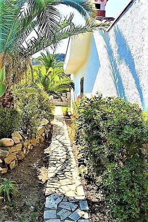 A stone pathway leading to a building with a blue exterior wall. - VILLA ROSA (Costa Rei)