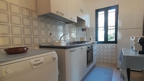 A compact kitchen with a dishwasher, stove, oven, and a window providing natural light.