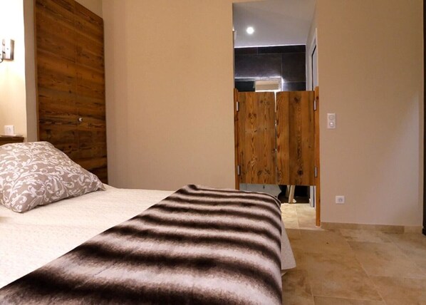 A bedroom with a bed, a wooden wardrobe, and a bathroom visible through an open door.