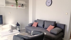 Ett modernt vardagsrum med en grå soffa, svarta fåtöljer, ett vitt soffbord, en tv och en väggklocka.