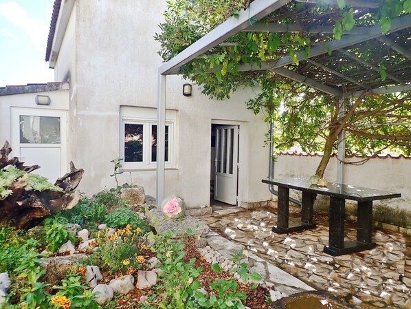 A courtyard with a stone floor, a pergola, a bench, and a variety of plants and flowers.