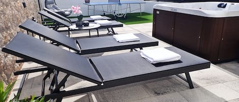 Eine Außenpatio mit Liegestühlen, einem Whirlpool und einem kleinen Tisch mit einer Pflanze.