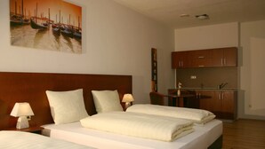 Habitación de hotel con dos camas, una kitchenette pequeña, un cabecero de madera y un cuadro de barcos en la pared.