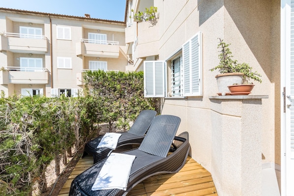 A balcony with two wicker lounge chairs, a wooden deck, and a potted plant.
