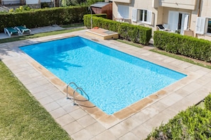 A rectangular swimming pool with a tiled deck, surrounded by a well-maintained lawn and hedges.