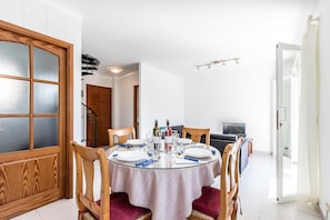 A dining area with a round table set for four, wooden chairs, and a sofa in the background.