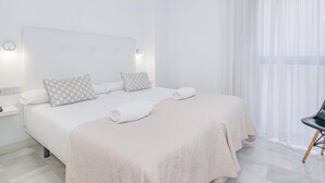 Hotellihuone, jossa on suuri sänky, kaksi yöpöytää, tuoli ja suuri ikkuna, jossa on ohuet verhot.