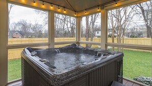 Un bain à remous situé dans un espace extérieur abrité, doté de grandes fenêtres et illuminé de guirlandes lumineuses.