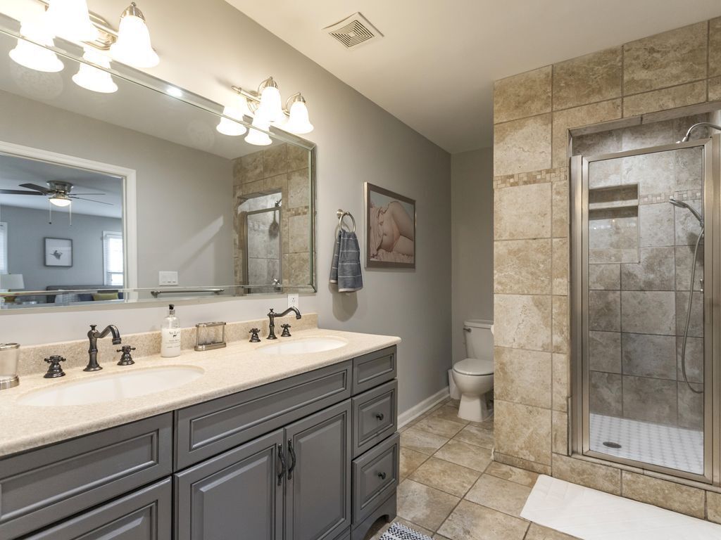 Une salle de bain avec un meuble-lavabo à deux vasques, un grand miroir, une cabine de douche et des toilettes.