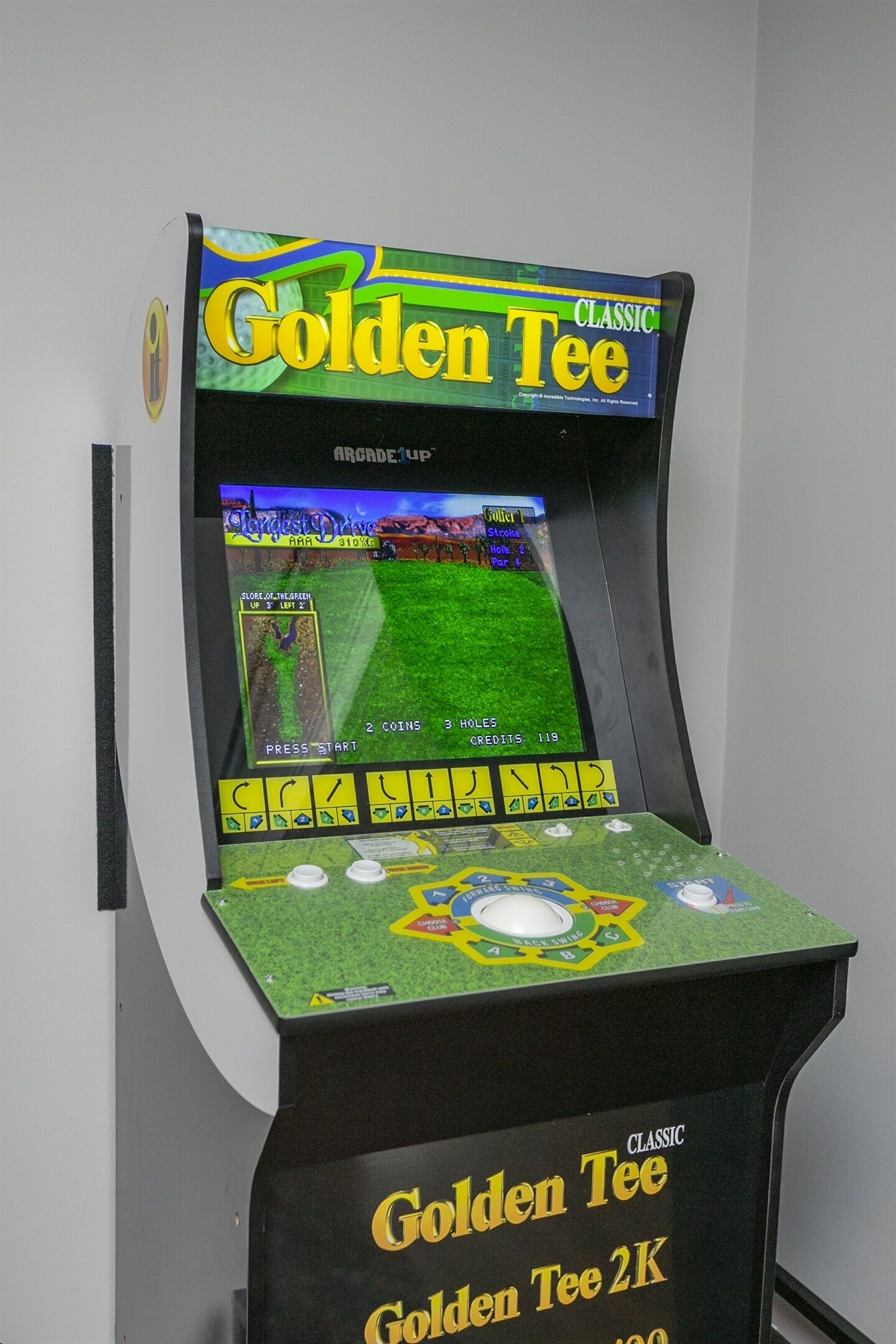 Une borne d’arcade ancienne, intitulée « Golden Tee », dotée d’un écran de jeu vert et d’un tableau d’affichage des scores.