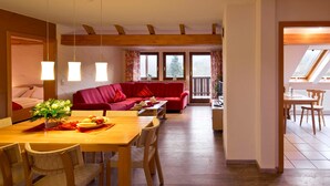 A dining area with a wooden table and chairs, a red sofa, and a balcony with a view. - Apartment 1 - Apartment am-edersee (Edertal)