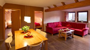 A cozy room with a wooden dining table, red sofa, and a bed in the background. - Apartment 1 - Apartment am-edersee (Edertal)