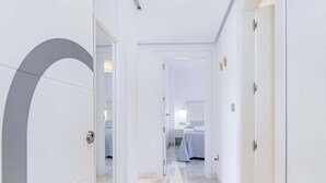 Un pasillo de hotel con diseño moderno, destacando una puerta con un tirador único, una cama visible en la habitación contigua y un piso limpio y con baldosas.