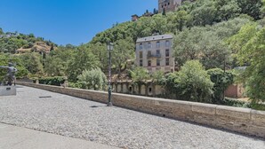 A cobblestone street with a statue, a stone wall, and a building with a tower.