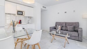 A modern living space with a glass dining table, white chairs, a grey sofa, and a kitchen area with white cabinets and a microwave. - Spacious and modern Apartment with free parking in the heart of Granada 10 (Granada)