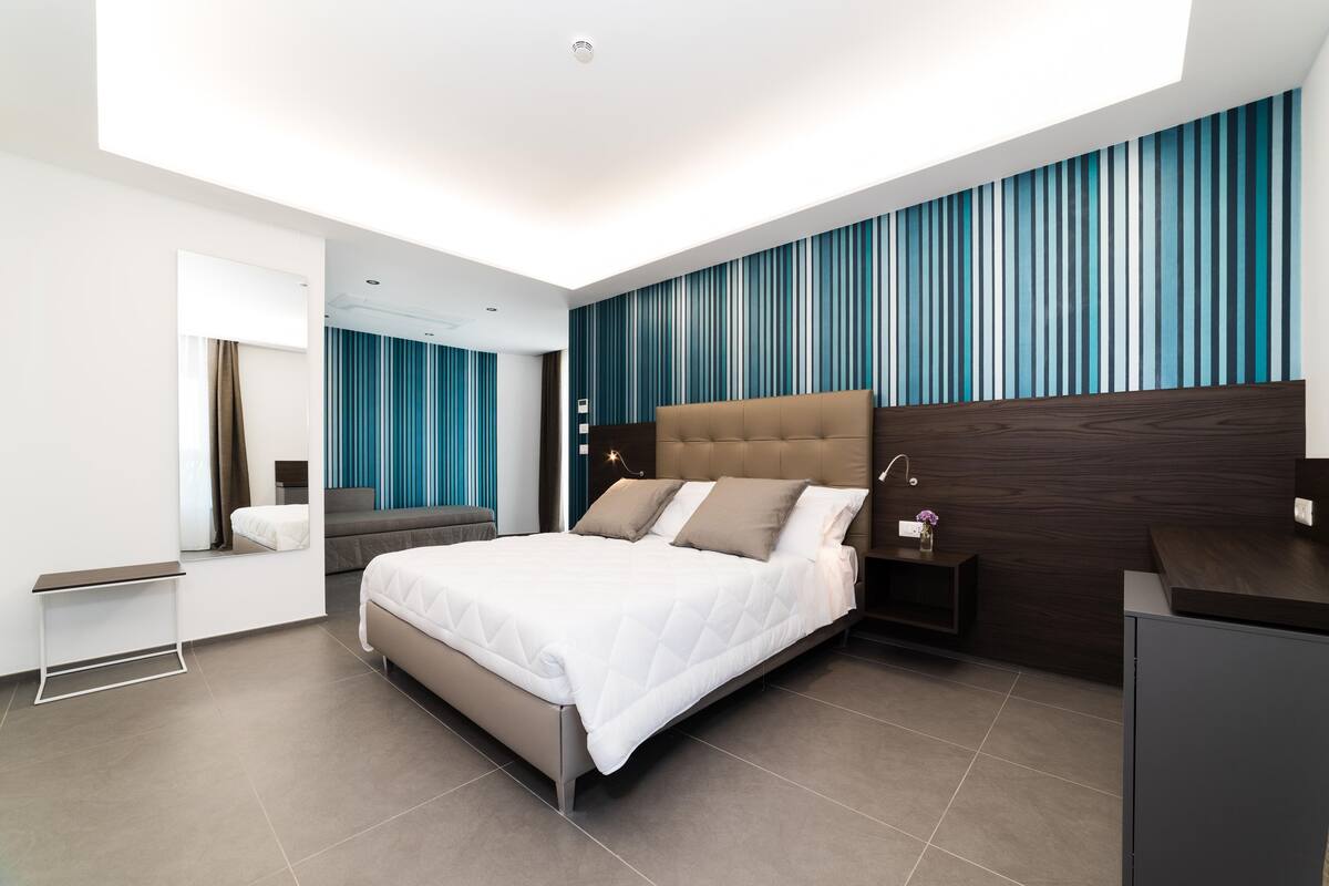 A modern bedroom with a large bed, a bedside table, a nightstand, and a mirror.
