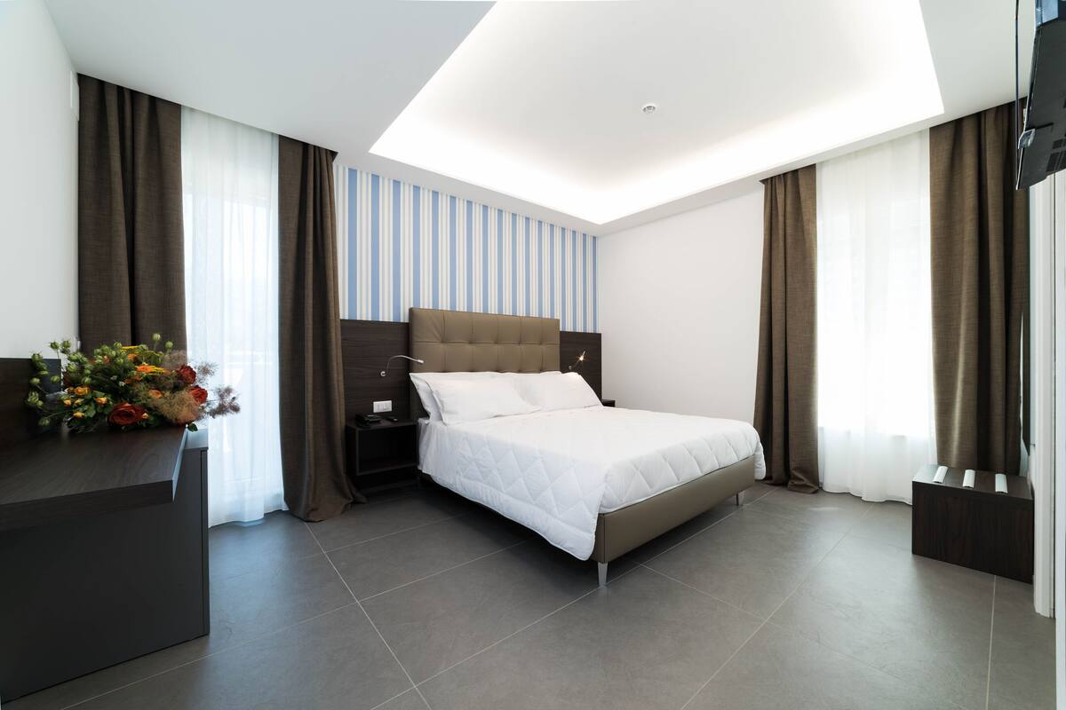 A modern hotel room with a large bed, a desk with a vase of flowers, and a flat-screen TV.