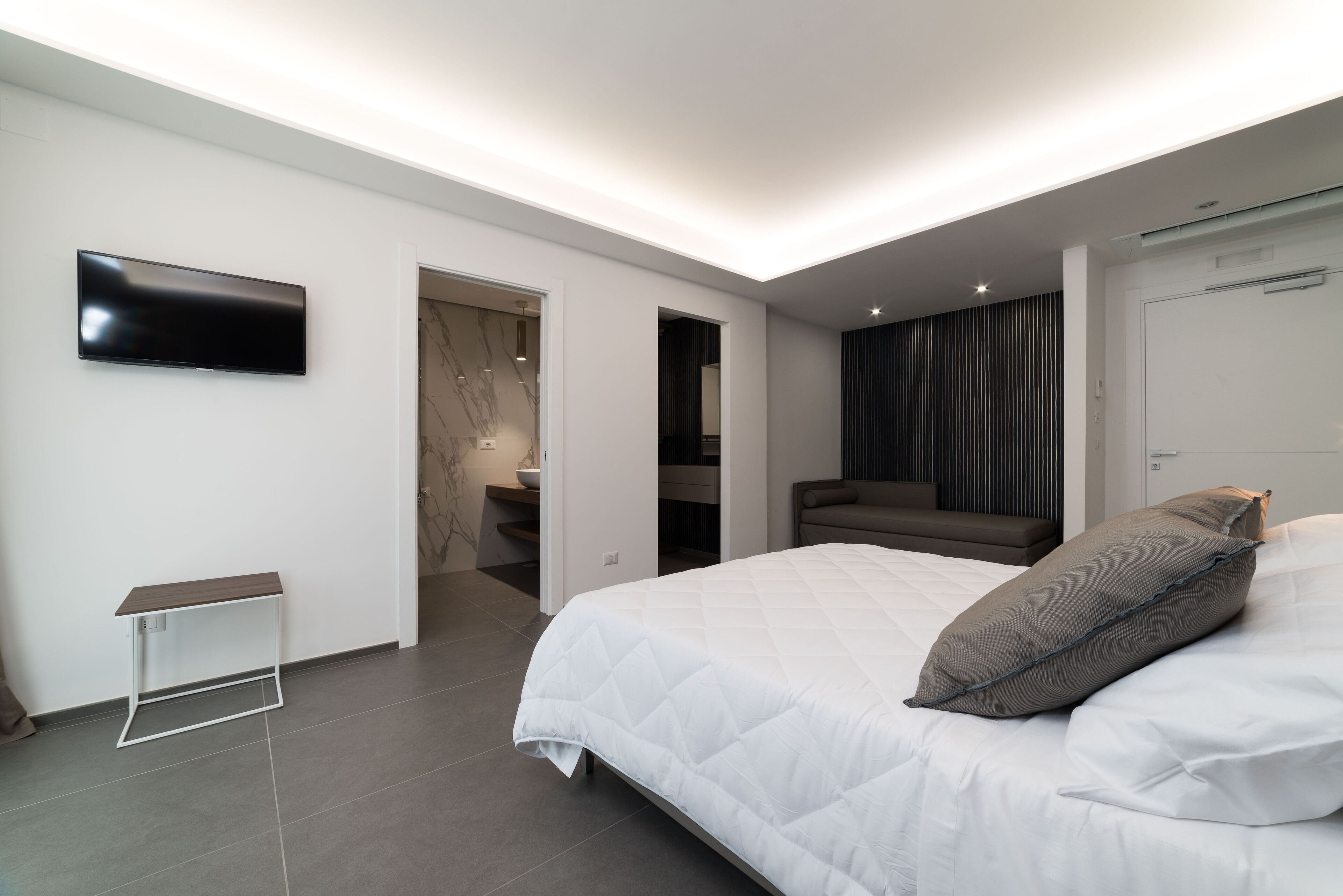 Camera da letto moderna con un ampio letto, una TV a schermo piatto montata a parete e un design minimalista.