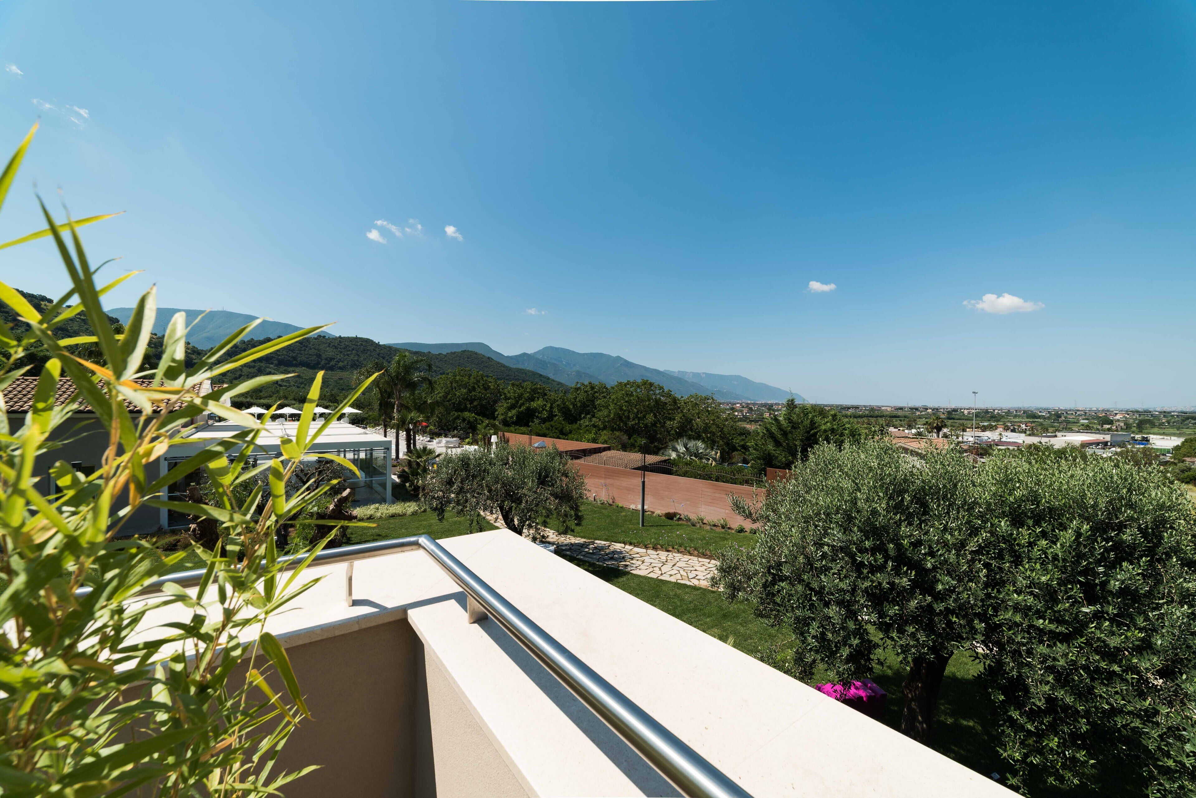 Un balcone con vista su un paesaggio montuoso, un'area giardino e un paese in lontananza.