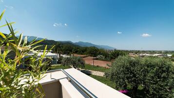 Un balcone con vista su un paesaggio montuoso, un'area giardino e un paese in lontananza.