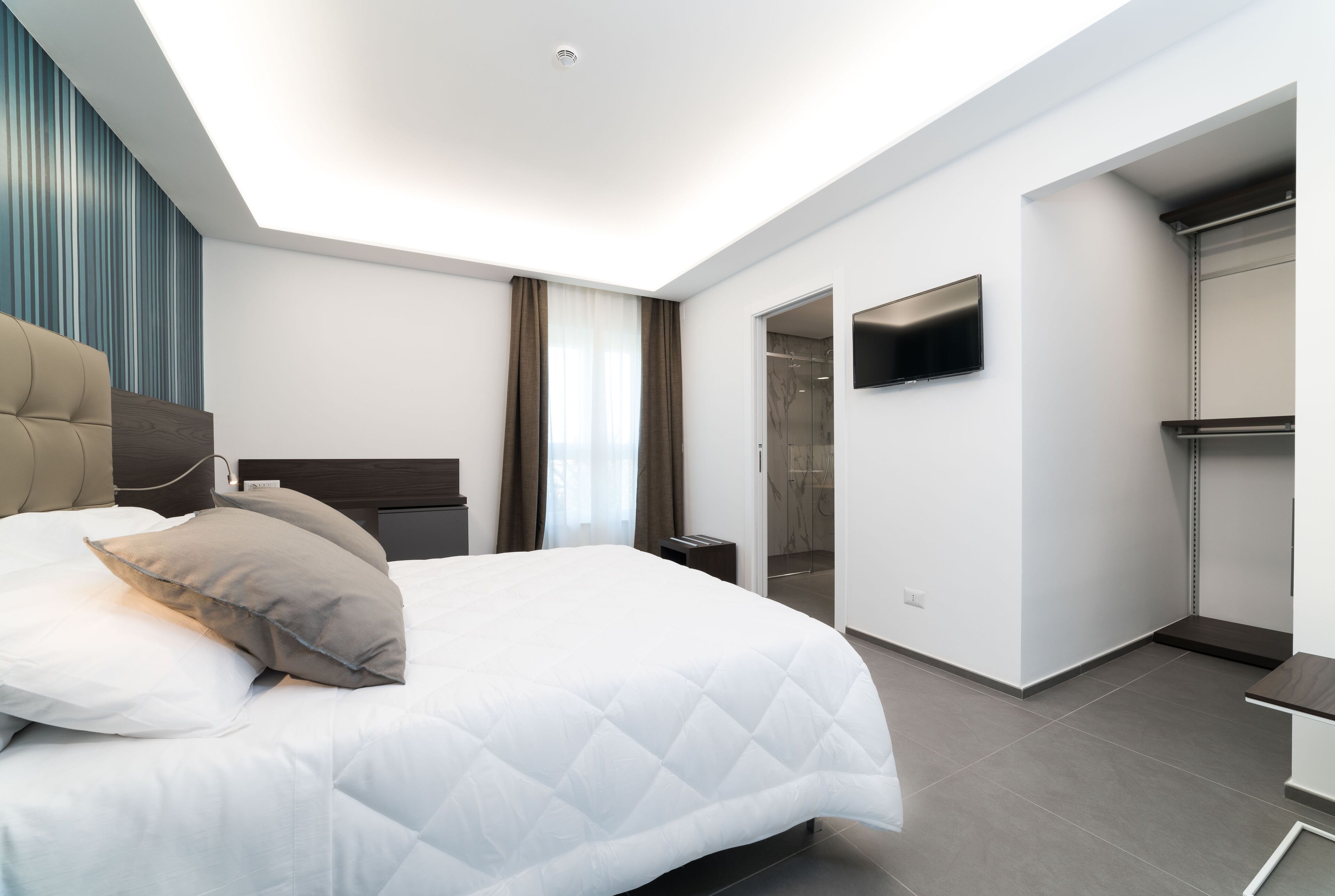 Une chambre à coucher moderne avec un grand lit, un téléviseur à écran plat fixé au mur et un dressing.