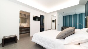 Une chambre à coucher moderne, avec un grand lit, une table de chevet, un miroir et une salle de bain visible à travers une porte ouverte.