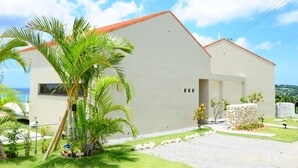 A modern building with a red roof, surrounded by a well-maintained lawn and palm trees. - Twin House Umigukuru (Nakijin)