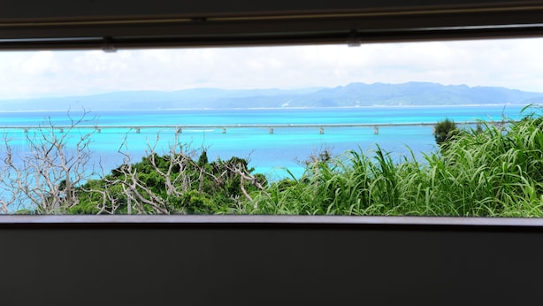 A view of a turquoise sea with distant mountains, viewed from a window with a metal frame. - Twin House Umigukuru (Nakijin)