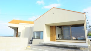 A modern two-story building with a flat roof, large windows, and a visible outdoor seating area. - Twin House Umigukuru (Nakijin)