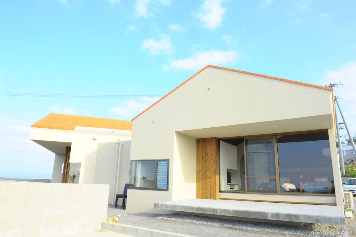 A modern two-story building with a flat roof, large windows, and a visible outdoor seating area.
