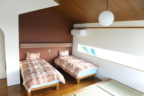 A bedroom with two beds, wooden flooring, a sloped ceiling, and a large window with a view. - Twin House Umigukuru (Nakijin)