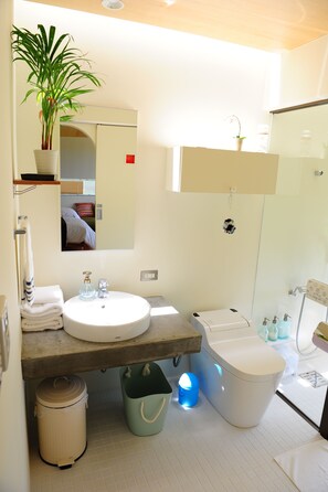 A modern bathroom with a round sink, a toilet, a mirror, and a potted plant. - Twin House Umigukuru (Nakijin)