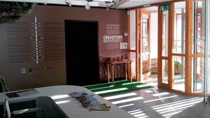 A modern interior with a reception desk, informational posters, and a glass door entrance. - Lizarrusti Parketxea - Hostel (Ataun)