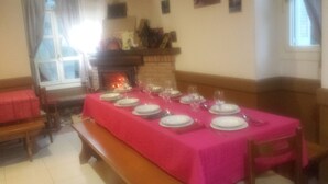 A dining room with a long table set for a meal, a fireplace, and a window with curtains. - Lizarrusti Parketxea - Hostel (Ataun)